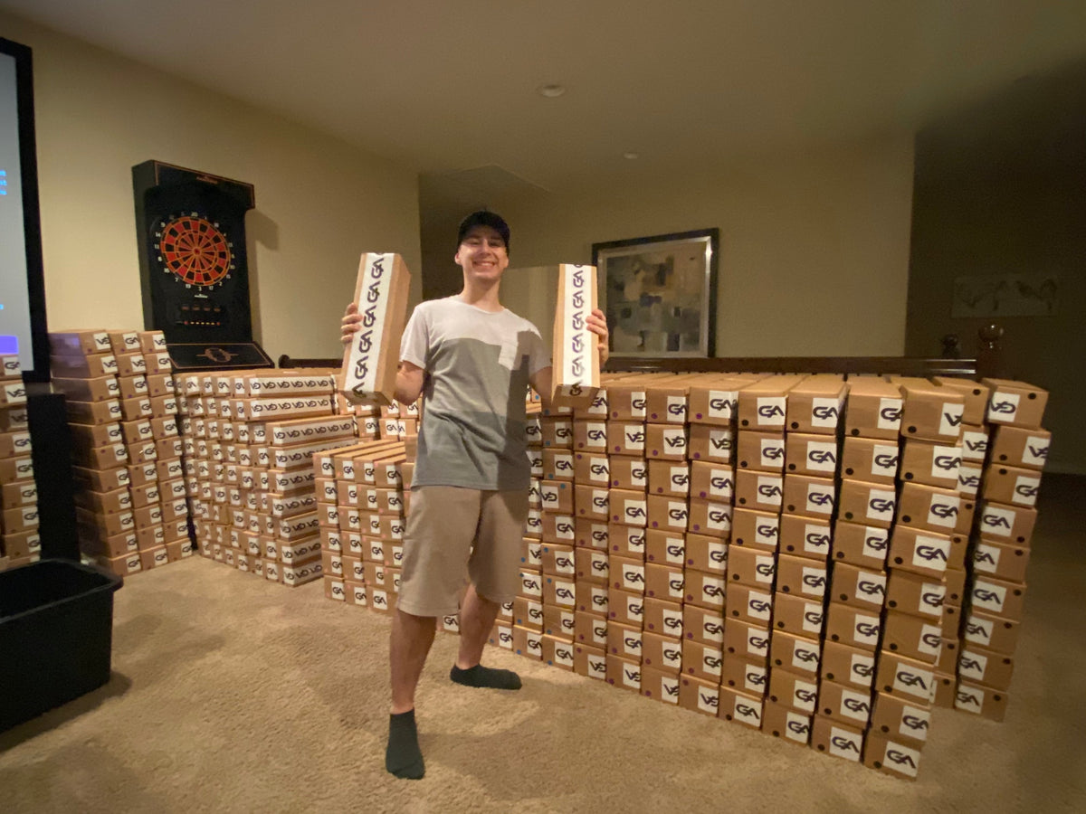 Aiden holding two GutzyAiden mousepad boxes in front of stacks of the first big order